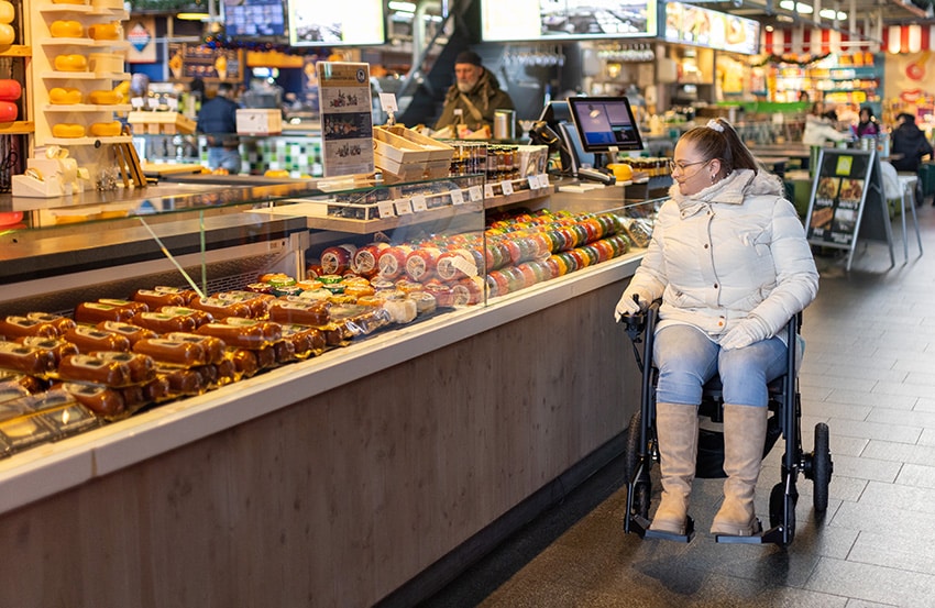 Femme conduisant un fauteuil roulant électrique Rollz Motion dans un marché